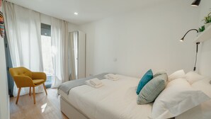 Una habitación de hotel con cama, una silla y ventana con cortinas.