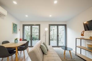 Un salon moderne avec un canapé, une table à manger, des chaises et un téléviseur posé sur une étagère.