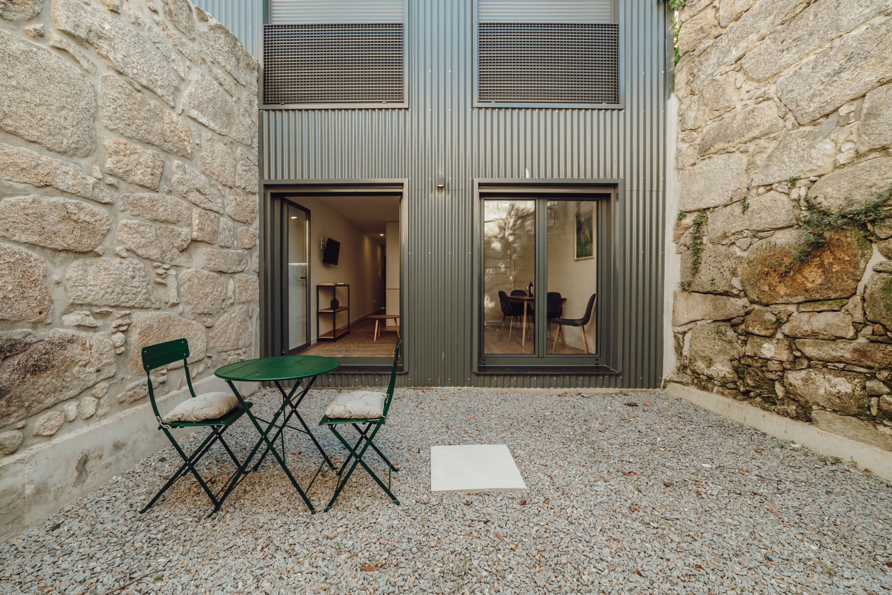 A stone building with a modern design, featuring a small outdoor seating area with a table and chairs.
