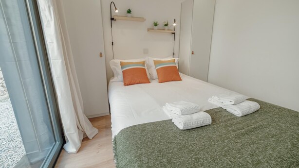 A neatly made bed with white linens and two orange pillows, a green throw blanket, and two folded towels on the bed. - Courtyard Oporto Design Apartment L With Terrace (Porto)