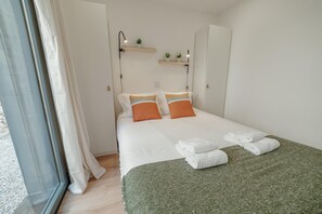 Ein ordentlich bezogenes Bett mit weißen Leinen, zwei orangefarbenen Kissen, einer grünen Tagesdecke und zwei gefalteten Handtüchern.