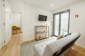 A modern living room with a sofa, a yellow chair, a TV, a console table, and a large window with a stone wall view. - Courtyard Oporto Design Apartment L With Terrace (Porto)