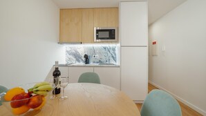 A compact kitchen with a microwave, sink, and a small countertop. There is a dining table with chairs and a fruit bowl. - Courtyard Oporto Design Apartment L With Terrace (Porto)