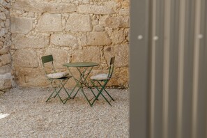 A small outdoor seating area with a stone wall backdrop, a round table, and two chairs.