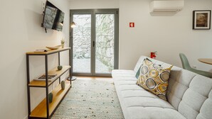 A living room with a sofa, a TV mounted on the wall, a bookshelf, and a door leading outside. - Courtyard Oporto Design Apartment L With Terrace (Porto)