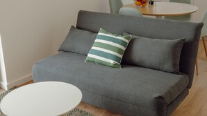 A grey sofa with a striped pillow, a round white table, and a dining area with chairs and a fruit bowl in the background. - Courtyard Oporto Design Apartment L With Terrace (Porto)