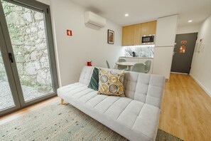 A modern living room with a sofa, a patterned pillow, a woven rug, a kitchen area with a microwave, and a door with a sign. - Courtyard Oporto Design Apartment L With Terrace (Porto)