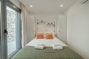 A modern hotel room with a large bed, two bedside tables, a window with curtains, and a stone wall outside. - Courtyard Oporto Design Apartment L With Terrace (Porto)