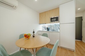 Eine kleine Küche mit Mikrowelle, Kühlschrank und einer Marmorarbeitsplatte. Ein Esstisch mit Stühlen und eine Schüssel mit Obst sind ebenfalls vorhanden.