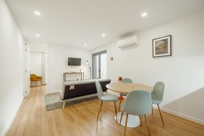 A modern room with a wooden floor, a round table with chairs, a sofa, a TV, and an air conditioning unit. - Courtyard Oporto Design Apartment L With Terrace (Porto)