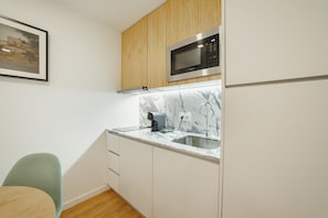 Una cocina compacta con microondas, cafetera y lavamanos.
