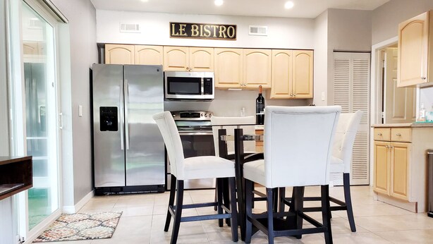 Una cocina moderna con comedor, que cuenta con electrodomésticos de acero inoxidable, armarios de tonos claros y un letrero que dice "LE BISTRO".