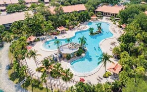 An aerial view of a resort with a large, winding pool surrounded by palm trees and lounge chairs. - An enchanting site, close to everything (Naples)