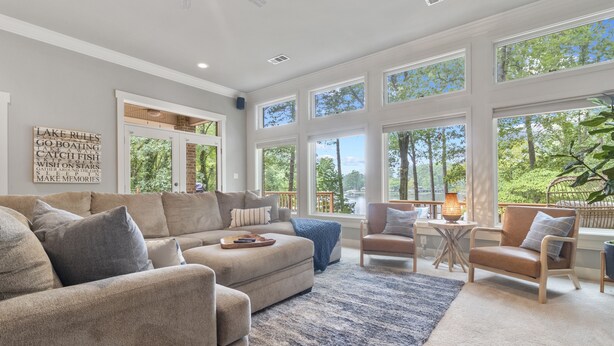 A spacious living room with a large sectional sofa, a small table with a lamp, and a view of the outdoors through large windows. - Lake Hamilton Waterfront Home Dock, Firepit, Sleeps 12 (Hot Springs)