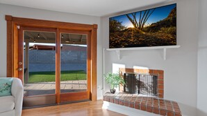Una sala de estar moderna con un ventanal corredizo que da a un patio, una chimenea y un televisor grande montado en la pared.
