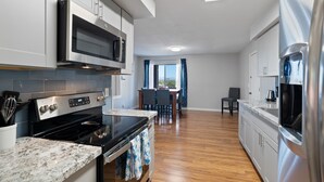Una cocina moderna con electrodomésticos de acero inoxidable, un comedor con mesa y sillas, y vistas a través de una ventana.