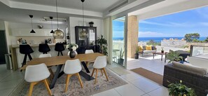 Une cuisine moderne avec un coin repas, une grande fenêtre donnant sur la mer et un balcon avec un espace salon extérieur.