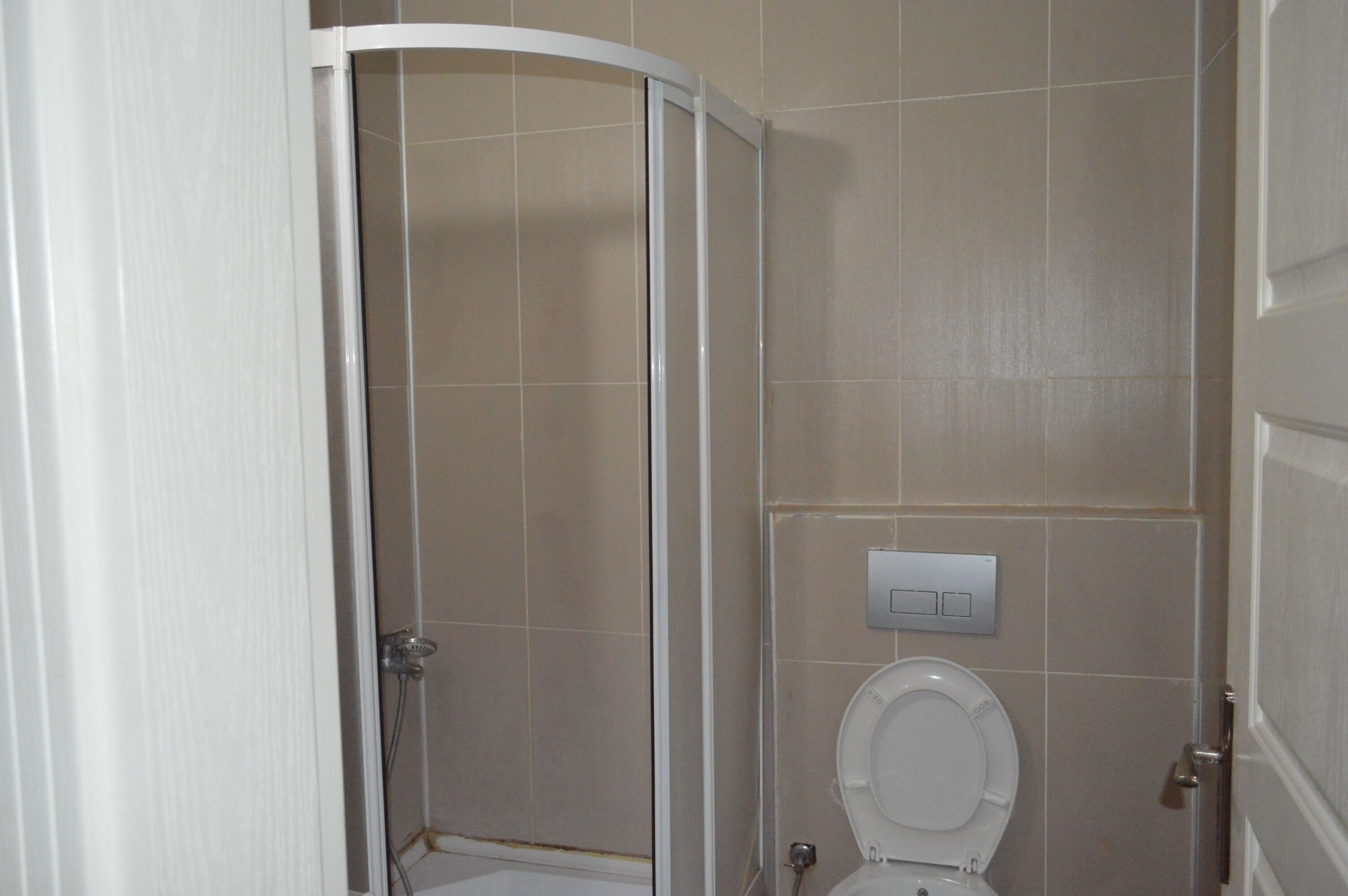 Un baño con cabina de ducha, inodoro y un interruptor de luz en la pared.