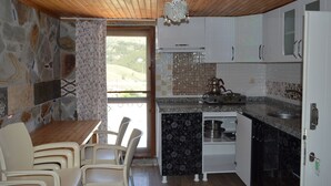 A compact kitchen with stone walls, a wooden ceiling, and a dining area with a table and chairs. - Koilada Konaklari (Gökçeada)
