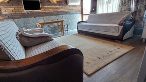 A living room with a sofa, a coffee table, and a TV mounted on the wall. - Koilada Konaklari (Gökçeada)