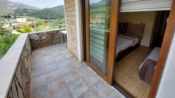 A balcony with a stone wall and a wooden door leading to a bedroom with a bed and a small table. - Koilada Konaklari (Gökçeada)