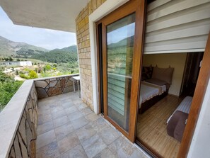 Un balcón con un muro de piedra y una puerta de madera que da a un dormitorio con una cama y una mesita.