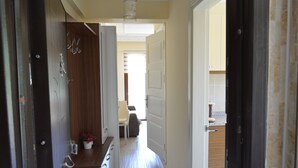 A hallway with a wooden door, a white door, and a view into a room with a chair and a small table. - Koilada Konaklari (Gökçeada)