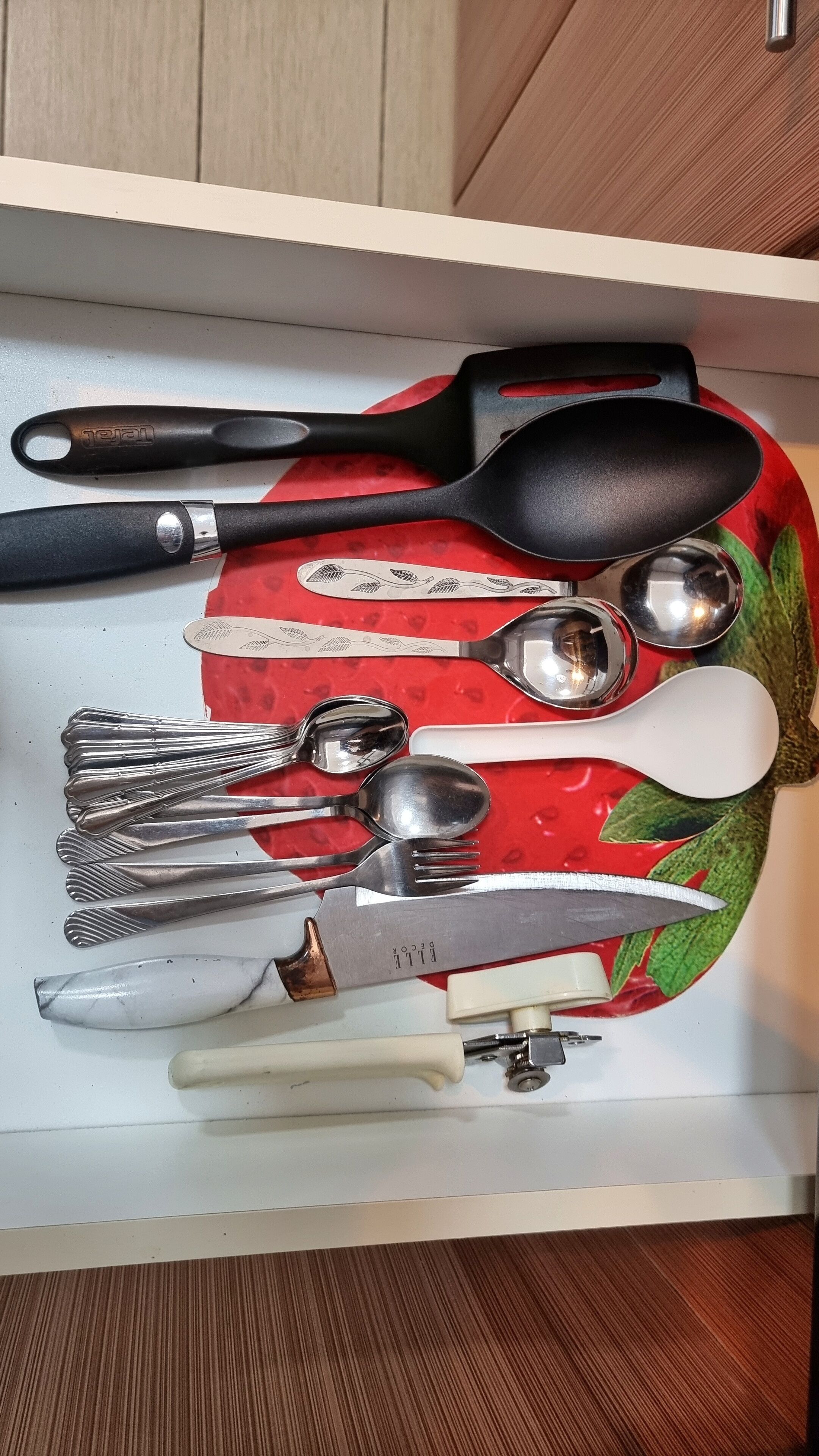 A drawer containing various kitchen utensils including a spatula, spoon, fork, knife, and a decorative plate.
