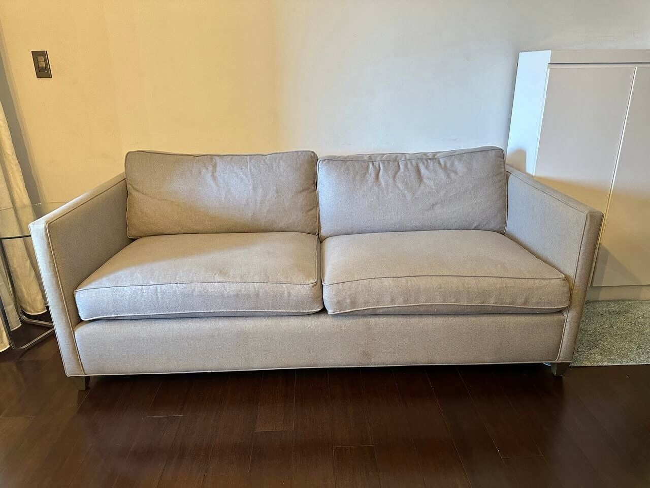 A beige sofa in a room with wooden flooring and a plain wall.