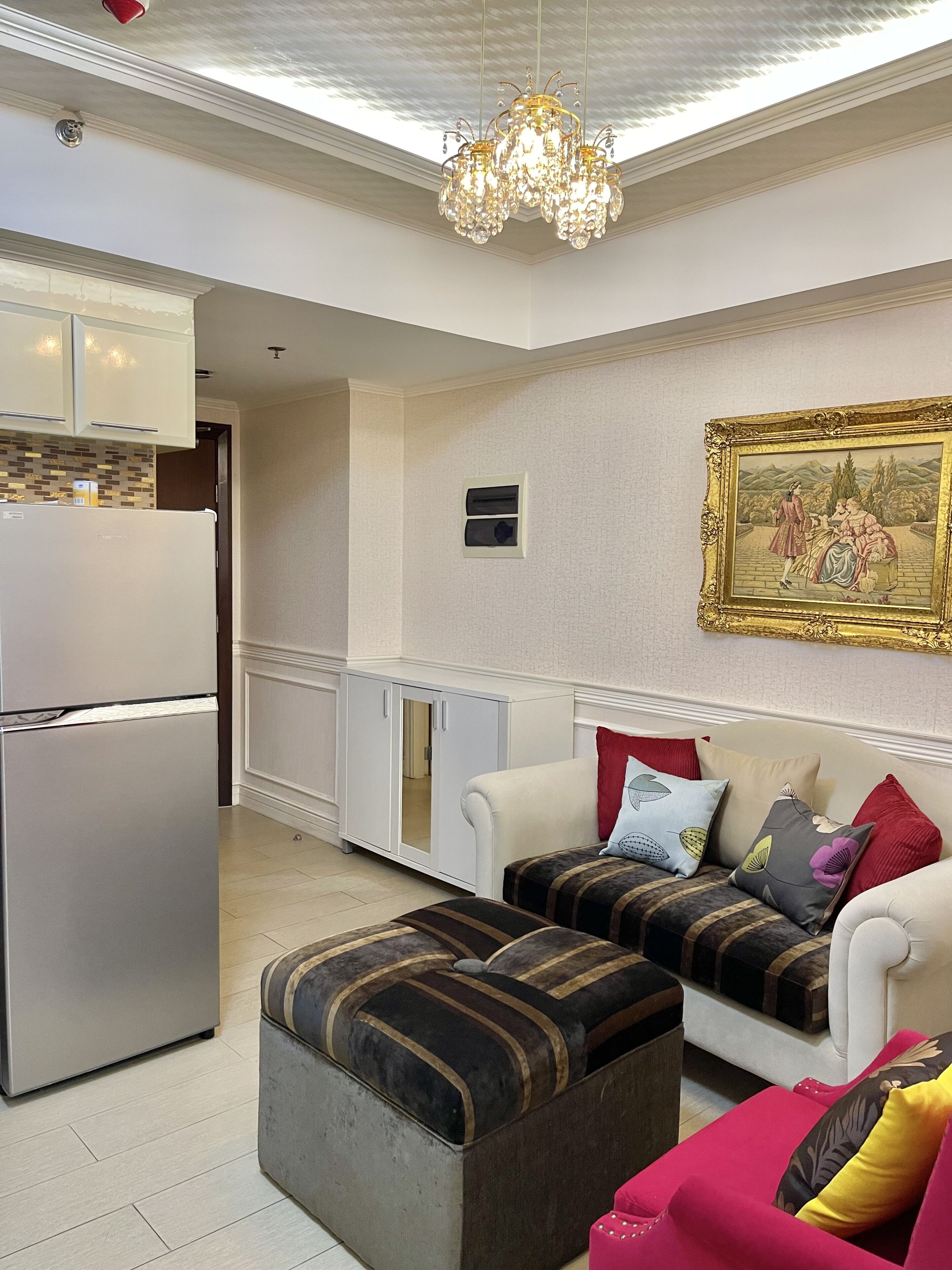 A modern living room with a sofa set, ottoman, and a dining area with a refrigerator.