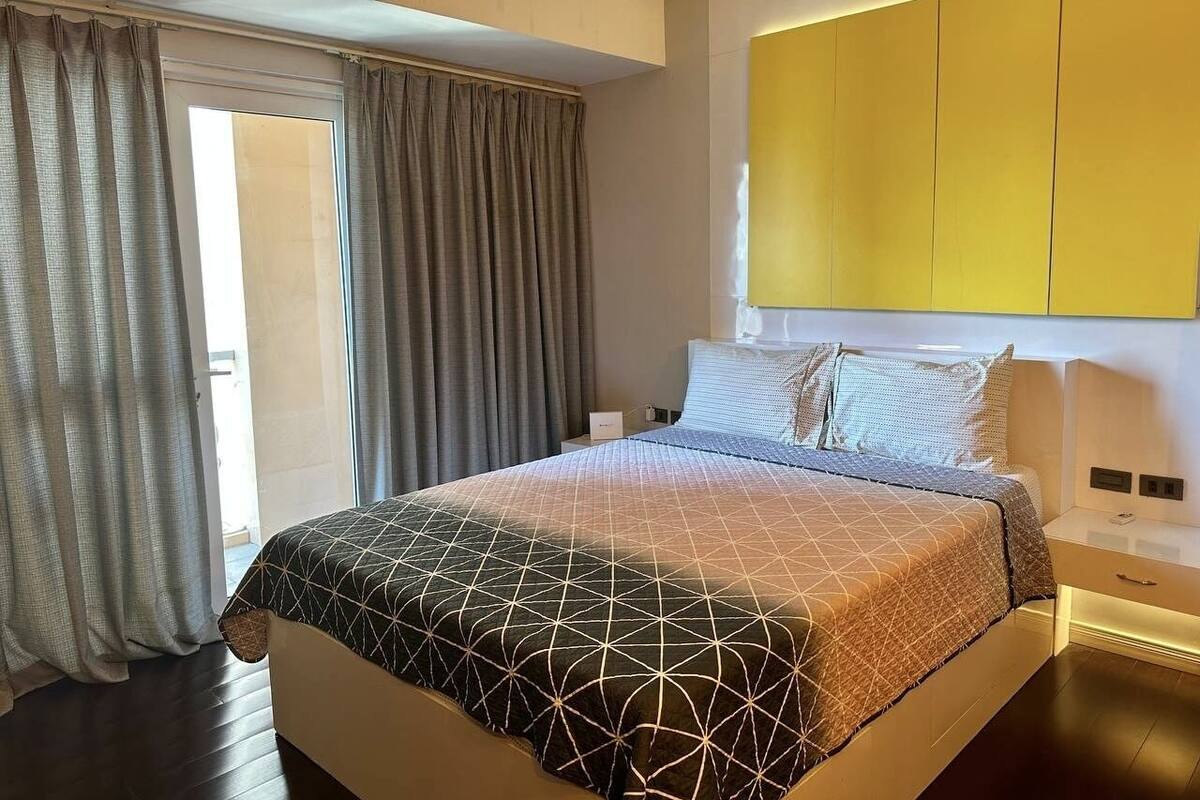 Moderni hotellihuone, jossa on suuri sänky, yöpöytä, yölamppu ja keltainen vaatekaappi.