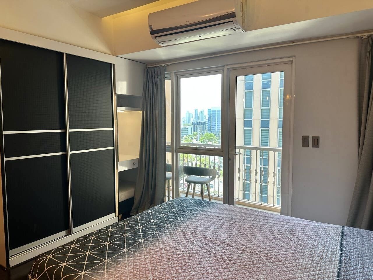 A hotel room with a bed, a wardrobe, a balcony with a chair, and a city view.
