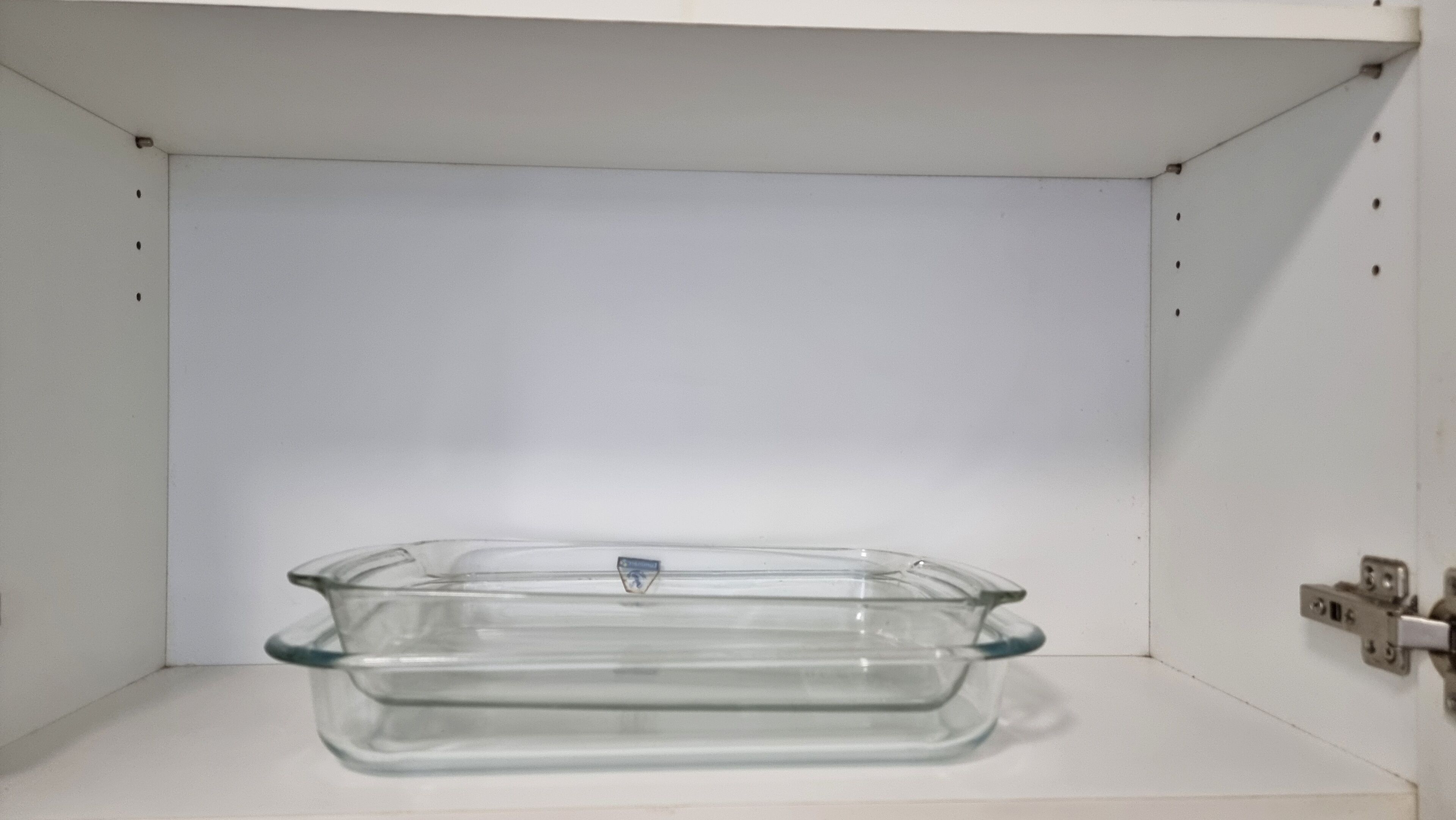 A clear glass dish on a white shelf.