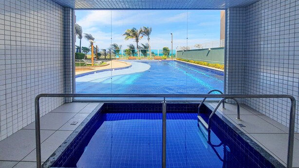 A swimming pool with a view of palm trees and a clear sky. - Beach Way Moderno Pé na Areia 2 quartos 5 pessoas By DM Apartments (Aquiraz)