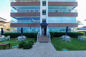 A multi-story hotel with a central entrance, outdoor seating area, and a well-maintained lawn. - Beach Way Moderno Pé na Areia 2 quartos 5 pessoas By DM Apartments (Aquiraz)