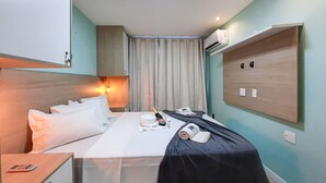 A hotel room with a bed, a bedside table, a lamp, a minibar, and a wall-mounted air conditioning unit. - Beach Way Moderno Pé na Areia 2 quartos 5 pessoas By DM Apartments (Aquiraz)