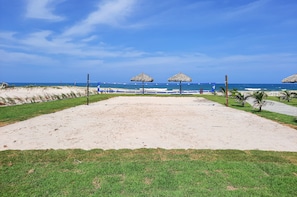 A beach with a sandy area, grass, and thatched umbrellas.