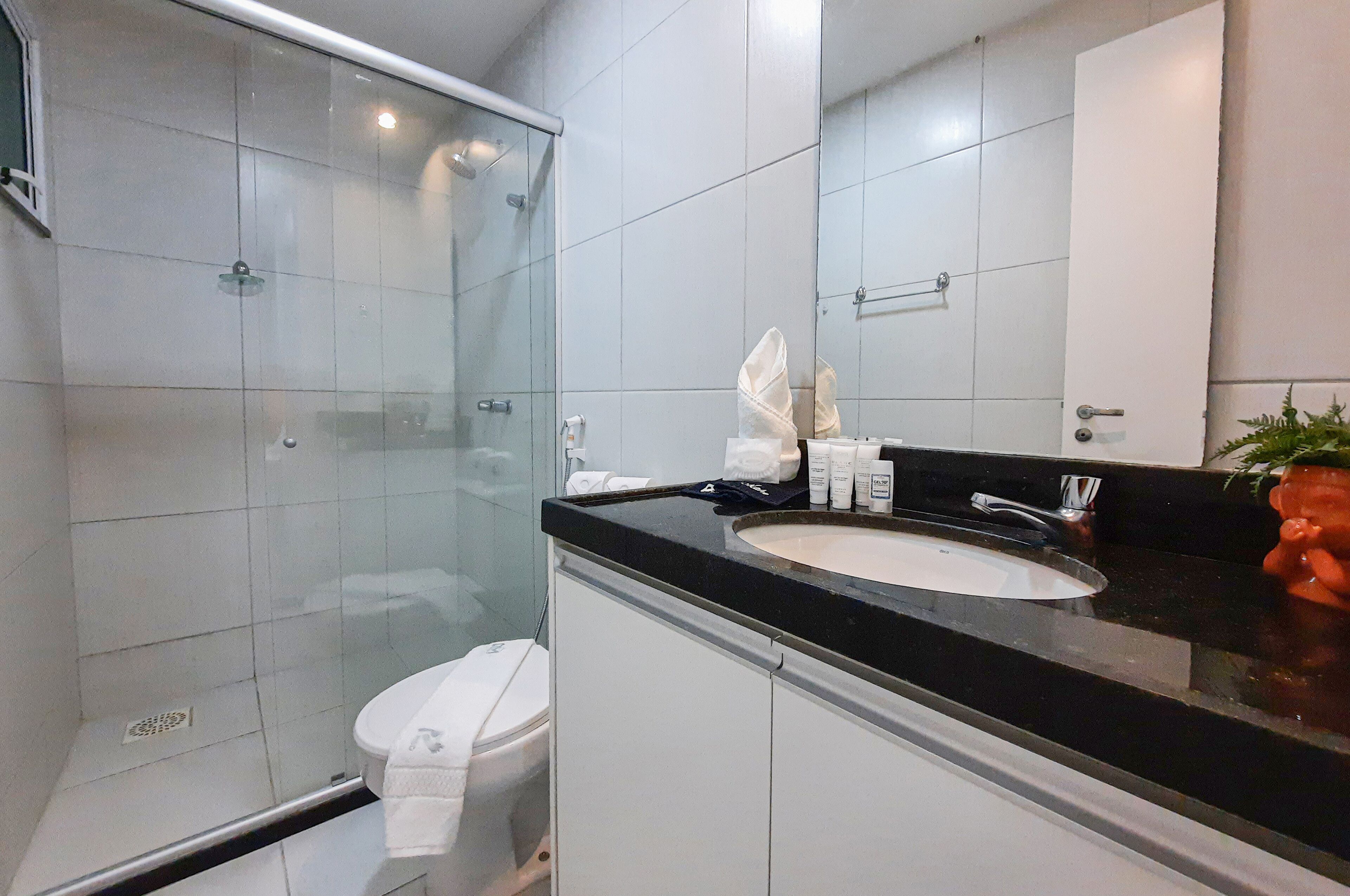 Une salle de bain moderne avec une douche à l’italienne en verre, des toilettes blanches, un lavabo noir et un miroir au-dessus.