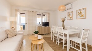 A modern living room with a sofa, dining table, chairs, a TV, and artwork on the walls. - Binilaya - Charming 3-bedroom house - seafront (Binibèquer Nou)