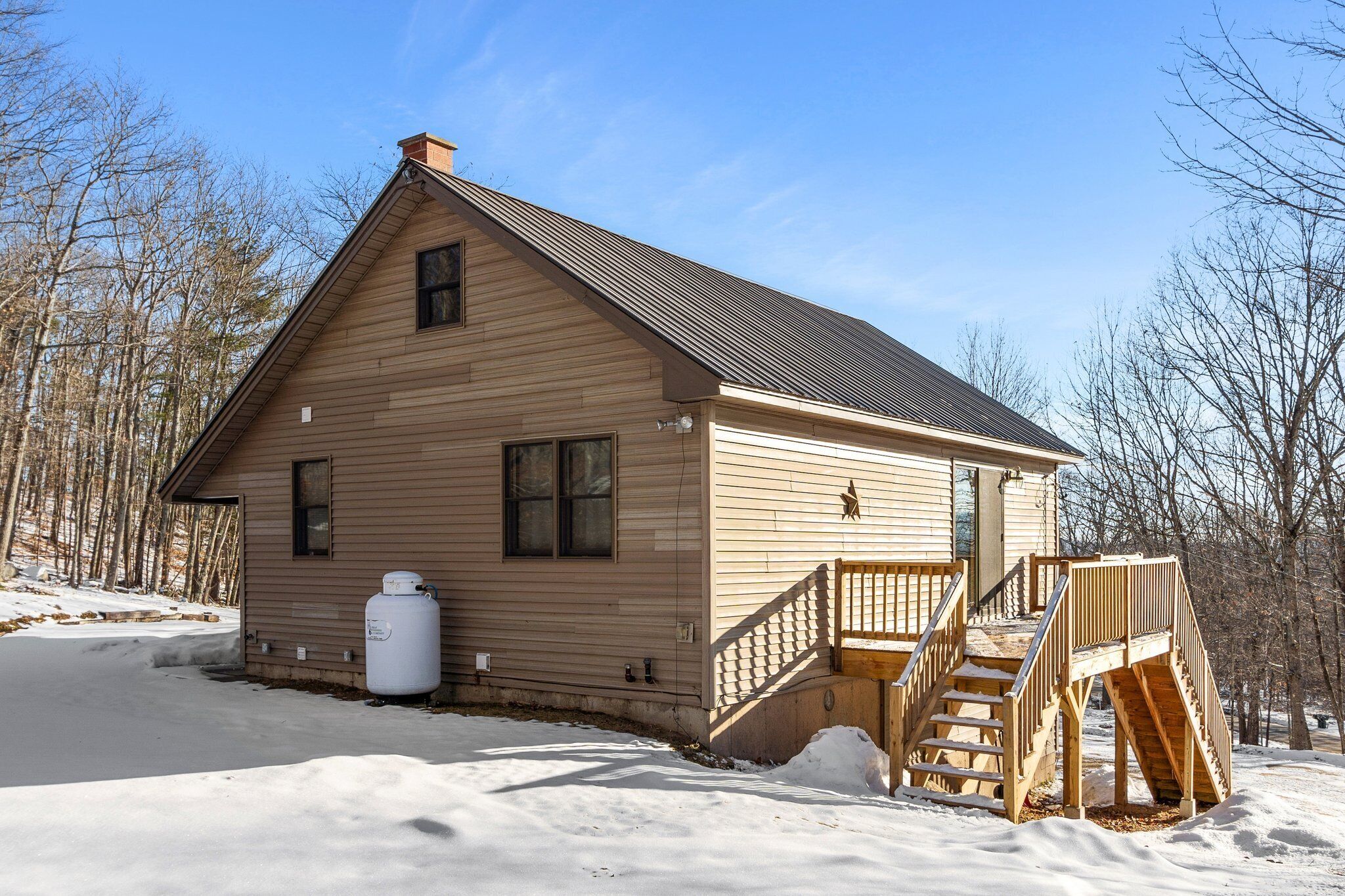 A wooden cabin with a metal roof, a small porch, and a staircase leading to the entrance.