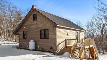 A wooden cabin with a metal roof, a small porch, and a staircase leading to the entrance.