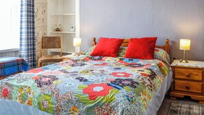 Een slaapkamer met een kleurrijke quilt, een houten nachtkastje, een stoel en een witte kledingkast.