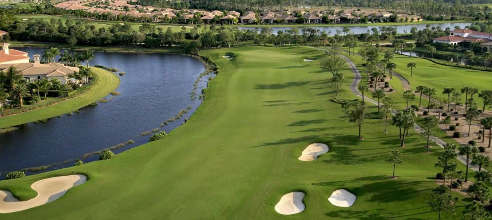 Un campo de golf con búnkeres de arena, un lago y edificios residenciales al fondo.