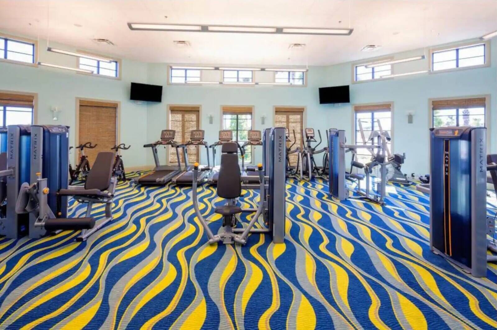 Ein Fitnessstudio mit Laufbändern, Kraftgeräten und einem gemusterten Teppich.