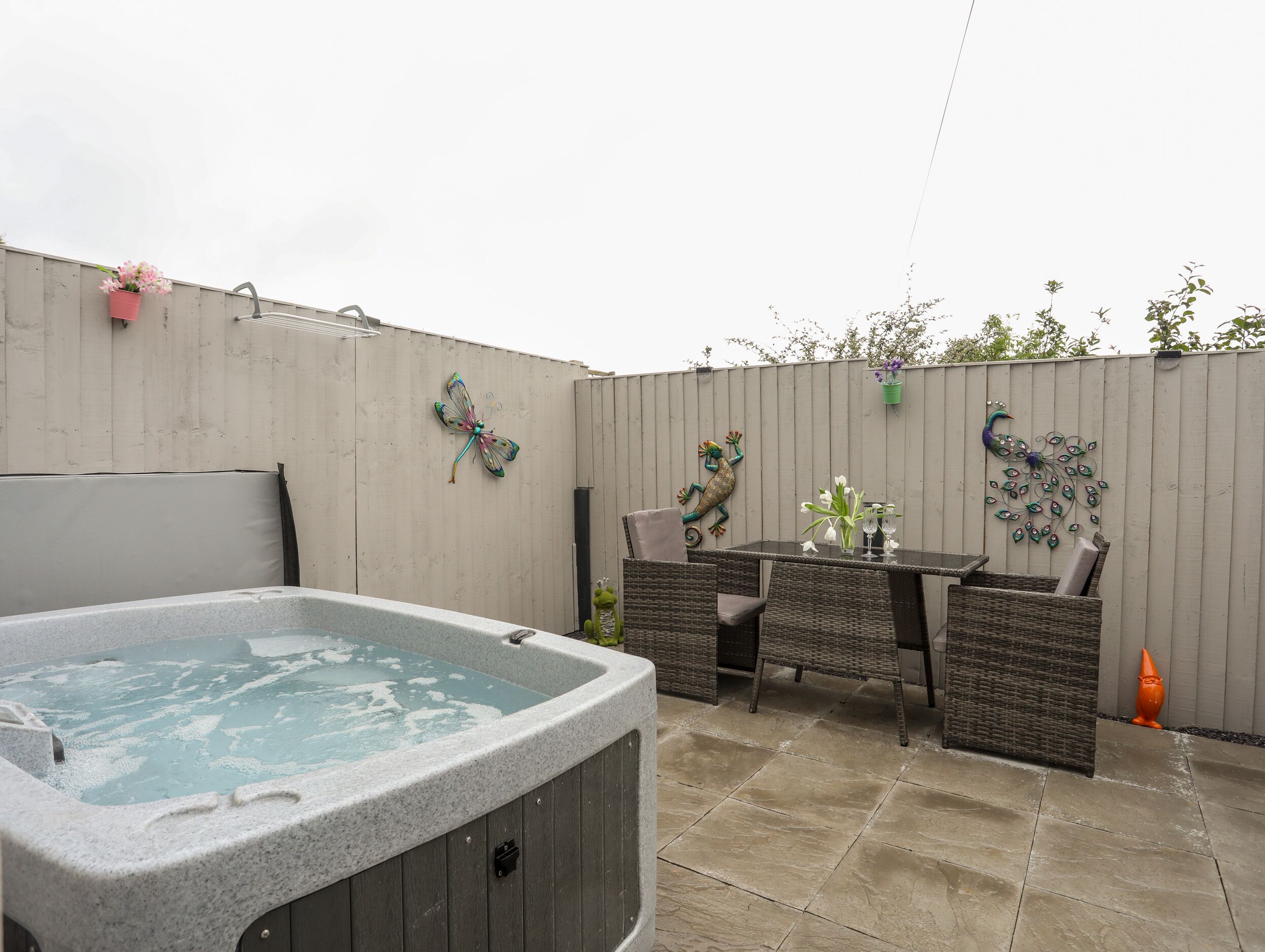 A backyard with a hot tub, wicker furniture, decorative wall art, and a tiled patio.