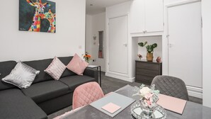 A modern living room with a black sofa, a dining table with chairs, a large painting on the wall, and a wardrobe. - Beeches Bach (Prestatyn)