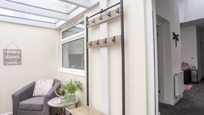 A modern room with a skylight, a grey armchair, a small table with a plant, and a wooden coat rack. - Beeches Bach (Prestatyn)