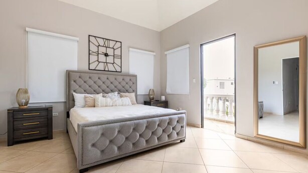 Une chambre avec un grand lit, une table de chevet, une commode, un miroir et un balcon avec vue.