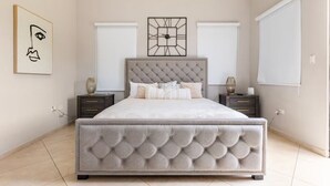 Une chambre à coucher avec une tête de lit capitonnée, un grand lit, deux tables de chevet avec des lampes et une horloge fixée au mur.