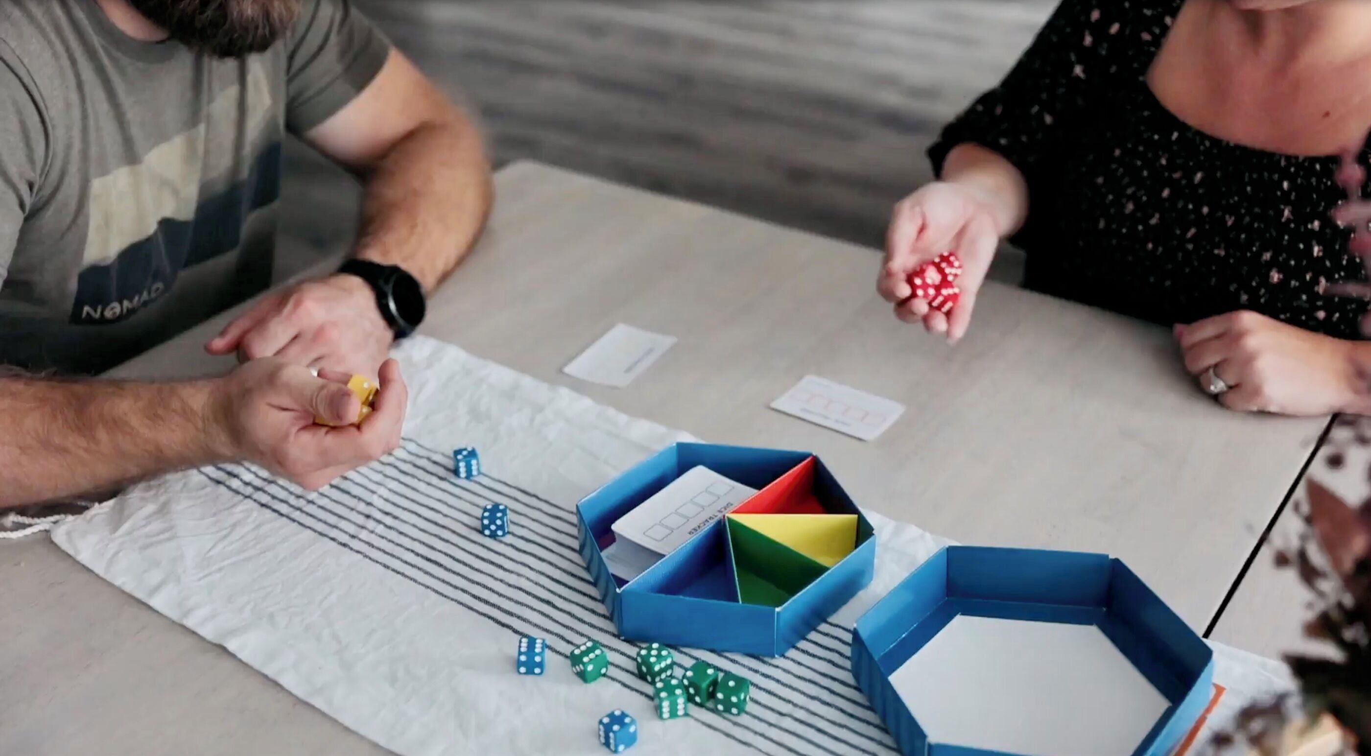 A person rolling a die on a table with dice and cards.